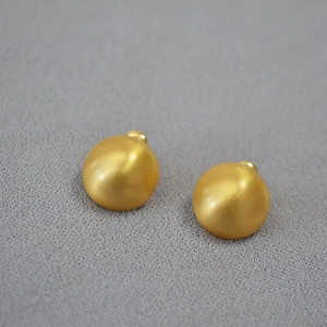 Detailed view of matte gold hemispherical stud earrings on grey textured fabric