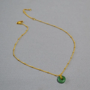 Gros plan d'un pendentif en jade vert sur chaîne satellite dorée avec fermoir mousqueton