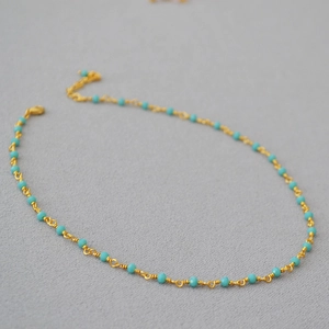 Detail of woven gold chain necklace with turquoise beads and lobster clasp closure