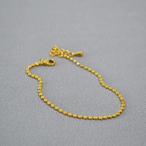 Detail of minimalist gold-plated bead bracelet with lobster clasp and drop pendant
