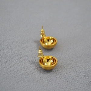 Close-up of golden hemispherical stud earrings with brushed texture on grey fabric