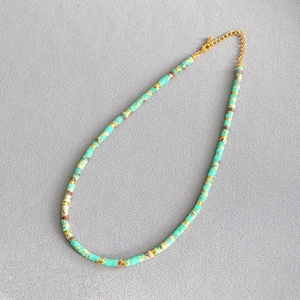 Detailed macro view of ocean-style green beaded necklace with gold metal spacers