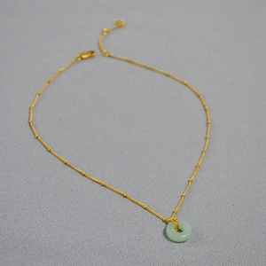 Détail d'un pendentif en jade vert clair sur une fine chaîne à billes dorée