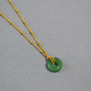 Détail du pendentif jade vert avec chaîne à perles dorées sur fond texturé gris foncé