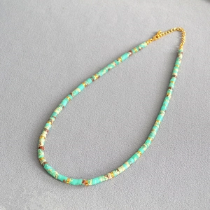 Detail of turquoise cylindrical beads and golden spacers on a textured grey background