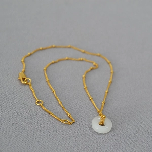 Gros plan du collier en laiton doré avec pendentif pingan-kou en jade blanc rond