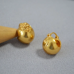 Macro shot of 3D lion head embossed gold sphere earrings on a textured backdrop