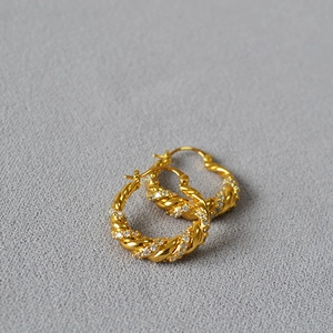Macro detail of golden twisted hoop earrings with shimmering pavé zircon stones
