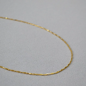 Macro shot of minimalist gold-plated brass chain necklace with textured wave design