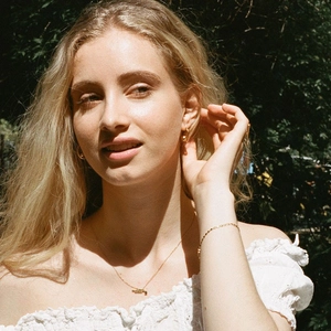 Detail of minimalist gold plated necklace and bracelet set worn outdoors in natural light