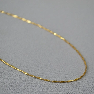 Detail of a minimalist gold-plated brass chain with flat rectangular links on grey fabric