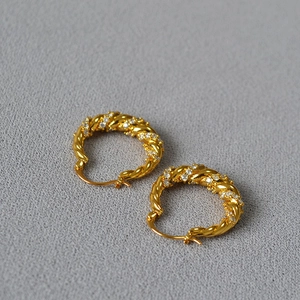 Detailed macro view of twisted gold hoop earrings with sparkling inlaid zircon stones