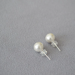Detailed view of matte white large faux pearl earrings on textured grey fabric
