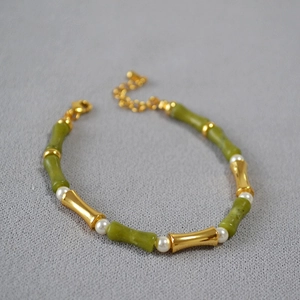 Detail of bamboo joint necklace with green jade-like beads and white pearls on grey fabric