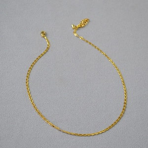 Detail of gold-plated brass lace chain necklace with lobster clasp on grey fabric