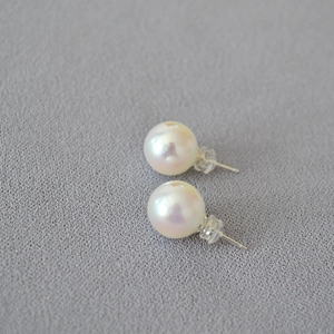 Close-up of elegant white round pearl earrings with 925 silver studs on grey fabric