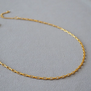 Détail d'un collier chaîne trombone en or mat avec fermoir mousqueton sur tissu gris