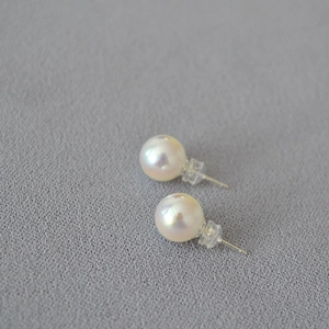 Macro view of high-luster faux pearl stud earrings with 925 silver pins on grey fabric