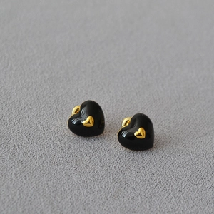 Detailed close-up of heart-shaped black enamel earrings with golden center accent