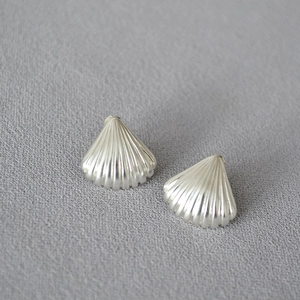 Macro shot of silver shell-shaped earrings with fan texture on grey fabric background