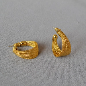 Detail of C-shaped gold plated earrings featuring a delicate mesh woven texture finish