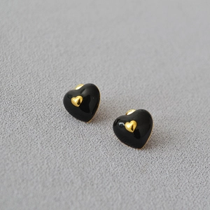 Elegant black enamel heart earrings with gold trim on a grey textured fabric background