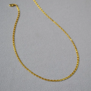 Detail of gold-plated brass chain with faceted texture and lobster clasp on grey fabric