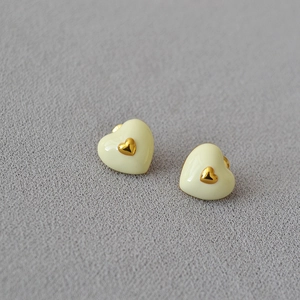 Elegant cream yellow enamel heart stud earrings with gold center on a gray textured background