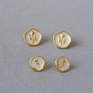 Détail macro de boucles d'oreilles tulipe et rose dorées avec émail blanc sur sable gris