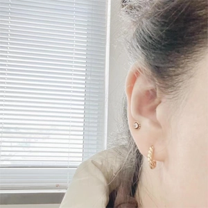 Close-up of golden flower stud with cubic zirconia and minimalist C-shaped hoop earring