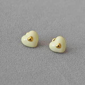 Close-up of beige enamel heart earrings with gold-plated studs on grey fabric