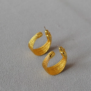 Textured gold C-shaped hoop earrings with intricate vintage pattern on neutral background