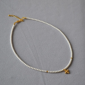 Minimalist faux pearl necklace with a gold cross star pendant on grey texture