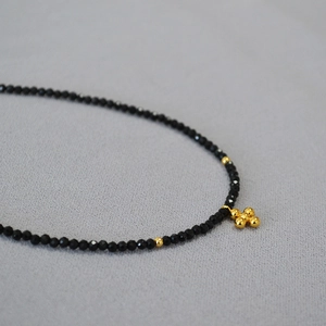 Dettaglio della collana di perline nere sfaccettate con ciondolo a croce dorata