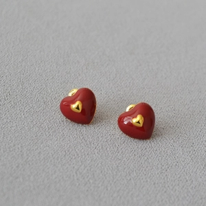 Detail of red enamel heart earrings with gold trim on a soft textured fabric background