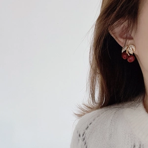 Macro view of cherry drop earrings with gold leaves and red stones on a model