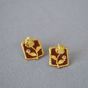 Detailed macro view of vintage brass gold earrings with red enamel rose and small zircon