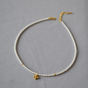 Detailed close-up of pearl necklace featuring gold cross pendant and lobster clasp detail