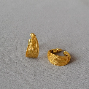 Detailed macro view of gold-plated C-shaped earrings with fine woven mesh texture