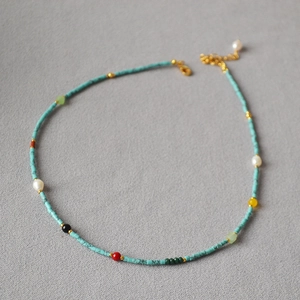 Detail of beaded turquoise necklace with pearls and golden lobster clasp on grey fabric