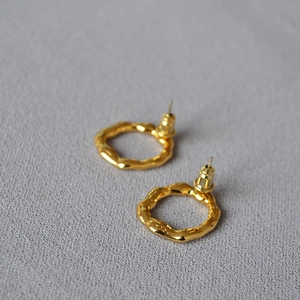 Minimalist gold-plated irregular wavy hoop earrings shown on light grey textured fabric