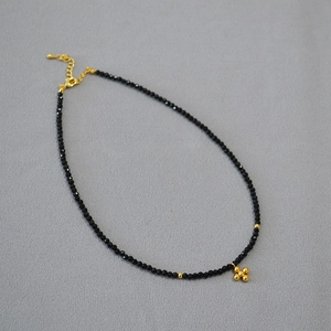 Dettaglio della collana di perline nere con ciondolo a croce dorata e chiusura a moschettone