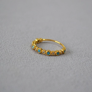 Macro detail of gold plated ring featuring inlaid blue turquoise and clear cubic zirconia
