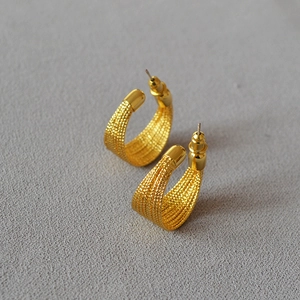 Detailed view of gold plated C-shaped hoop earrings with textured braided pattern