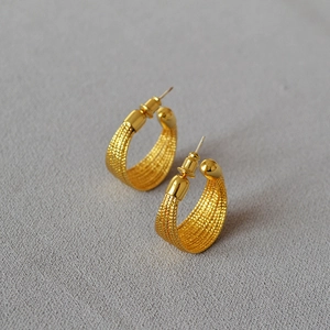 Close-up of gold-plated C-shaped earrings with intricate braided mesh texture details