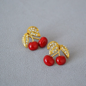 Detailed view of red cherry earrings with gold leaf accents and shimmering crystals