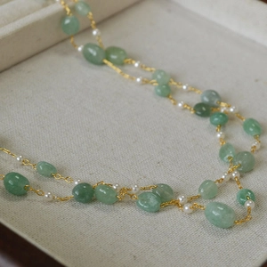 Detailed close-up of handmade necklace with green gemstones and small white pearls