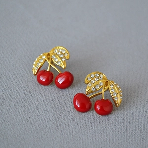 Detail of red cherry earrings with gold leaves and sparkling rhinestones on fabric