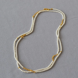 Detail of layered white pearl necklace with golden metal chains on grey fabric