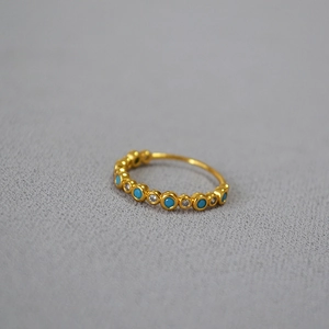Gold-plated brass ring with alternating turquoise and cubic zirconia gemstones on gray surface